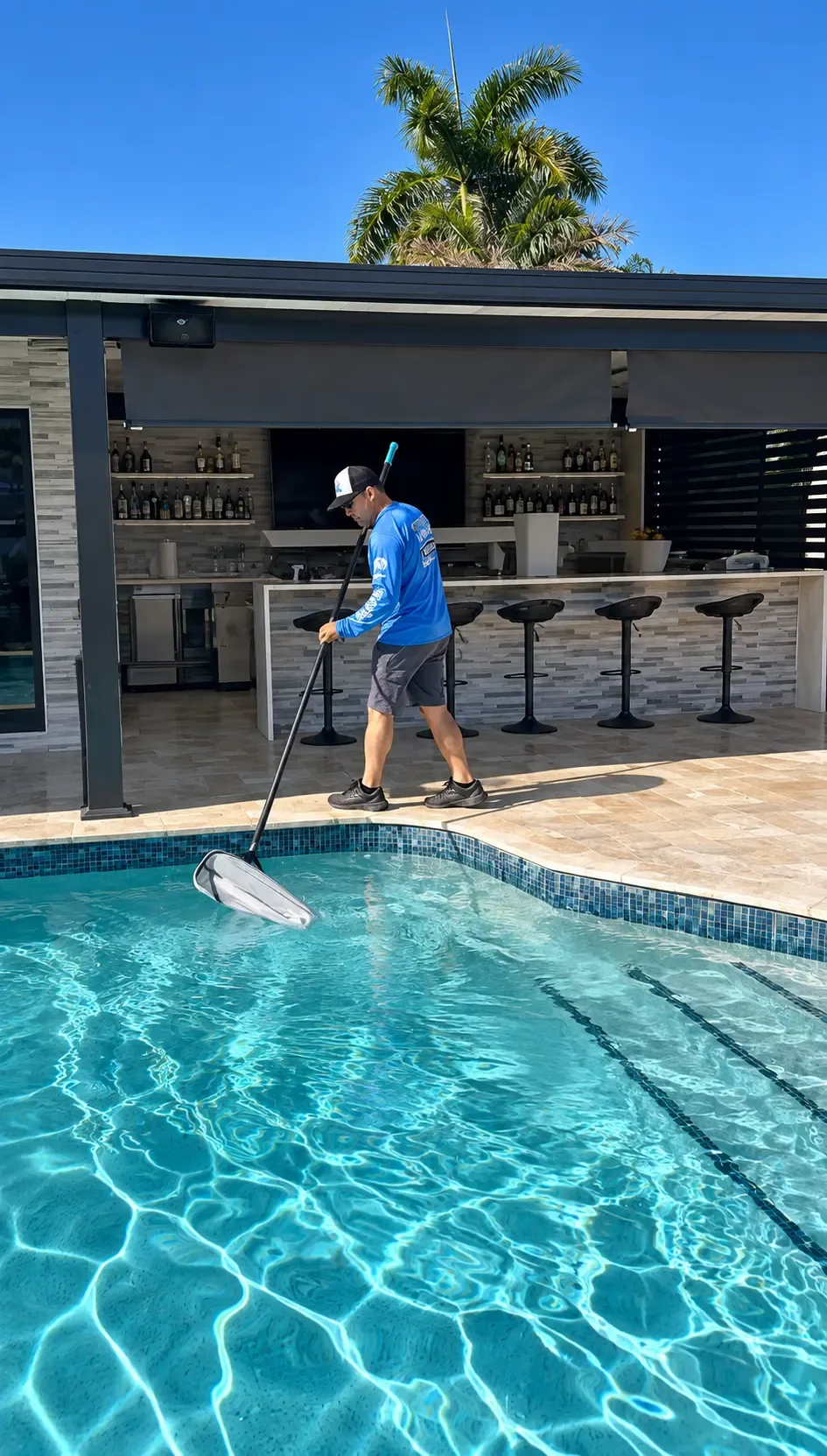 Alex Pool Cleaning technician skimming the surface of a pool beside an outdoor kitchen bar