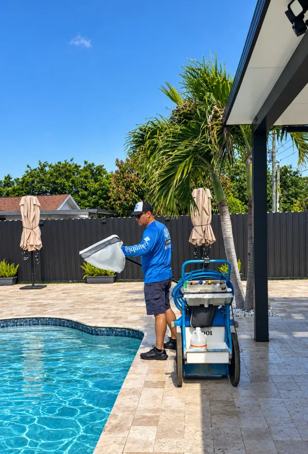 Technician emptying a skimmer net into a wheeled service cart beside a screened pool